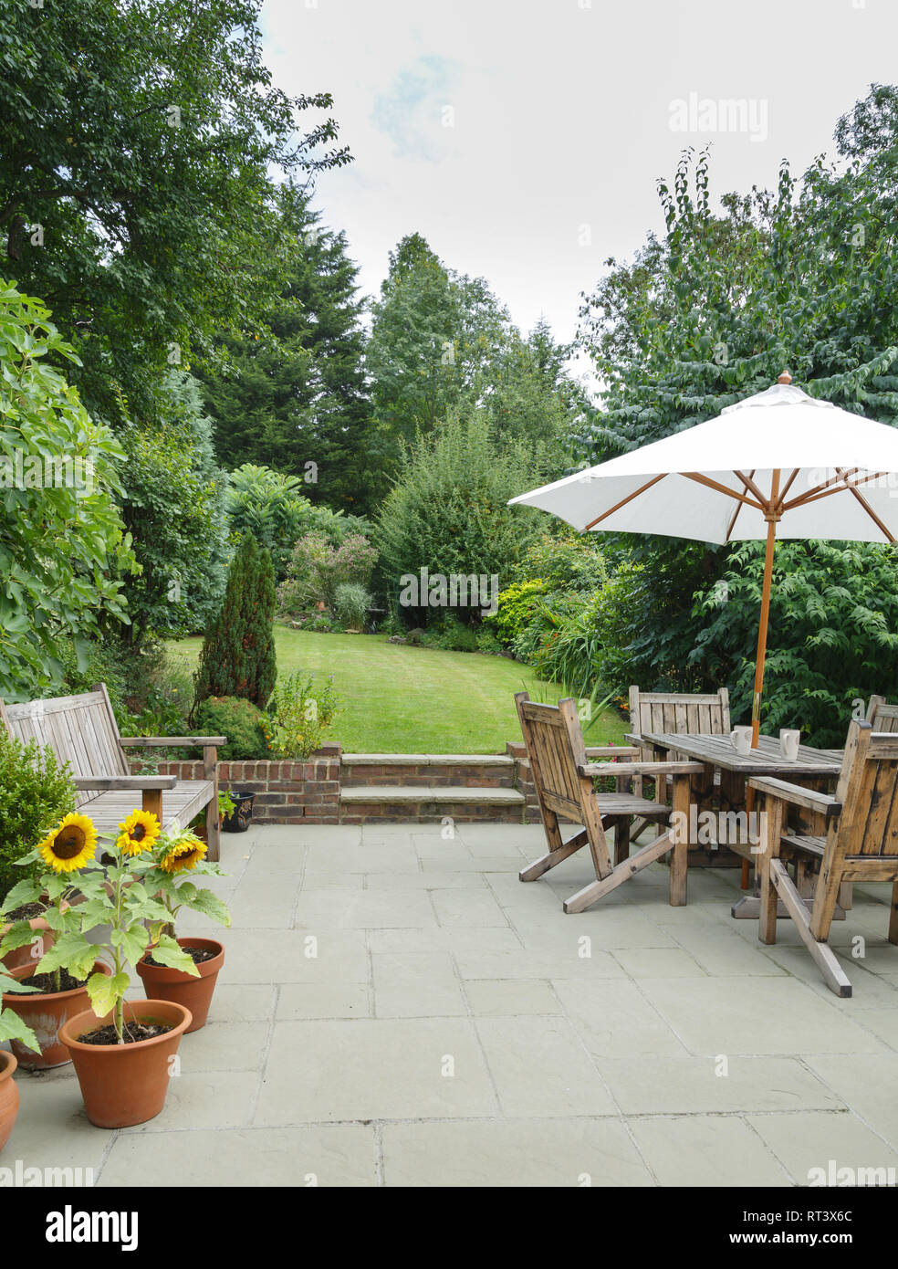 Garten im Sommer mit Terrasse, Gartenmöbeln und einem Sonnenschirm oder Sonnenschirm Stockfoto