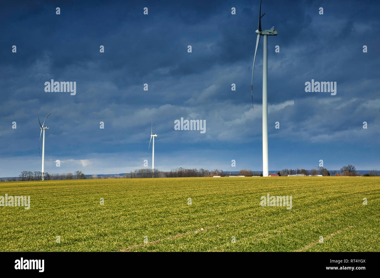 Drei Windmühlen für Stromerzeugung durch landwirtschaftliche Felder in Polnischen umgeben. Vor dem Hintergrund der schwere, schwarze Wolken Stockfoto