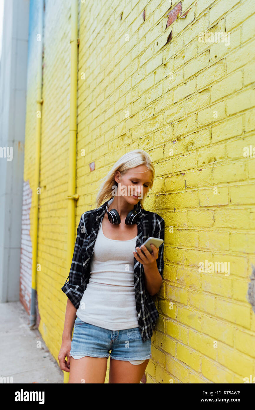 Junge Frau Kontrolle Handy im yellow brick wall Stockfoto