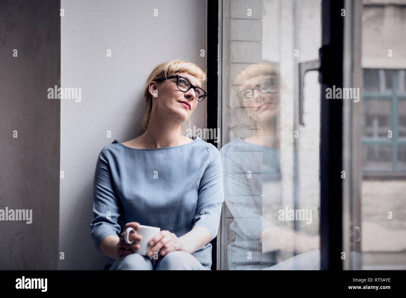 Porträt der lächelnde Frau mit kaffeebecher Blick durch Fenster Stockfoto