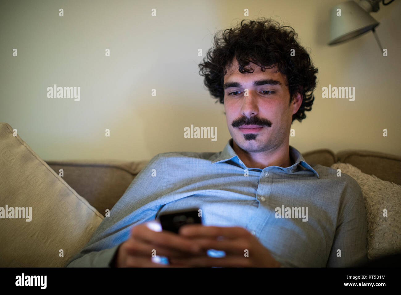 Mann mit Smart Phone auf einem Sofa in der Nacht Stockfoto