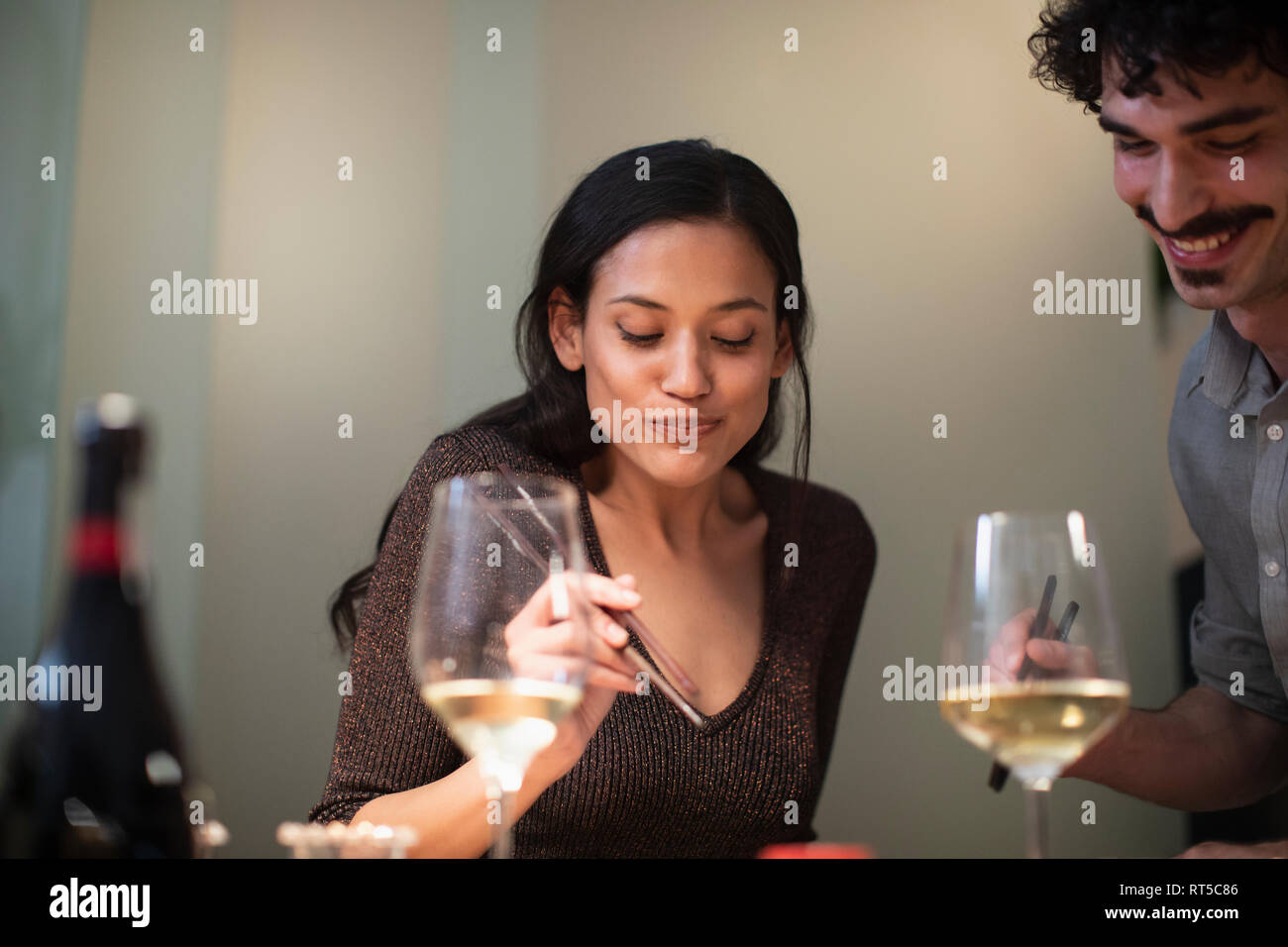 Lächelndes Paar mit Stäbchen Essen und Trinken Weißwein Stockfoto