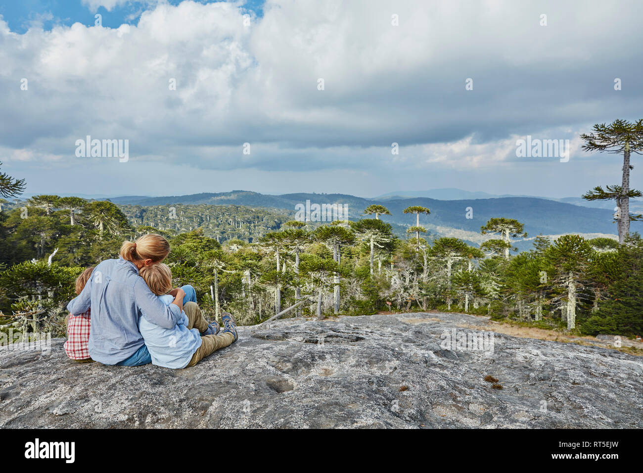 Chile, Puren, El Melado Nationalpark, Frau sitzt mit Söhnen auf Boulder bei Araucaria Forest suchen Stockfoto