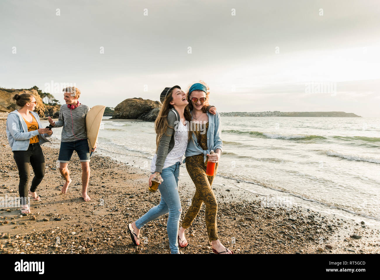 Gerne Freunde mit Surfbrett und Getränke gehen auf steinigem Strand Stockfoto