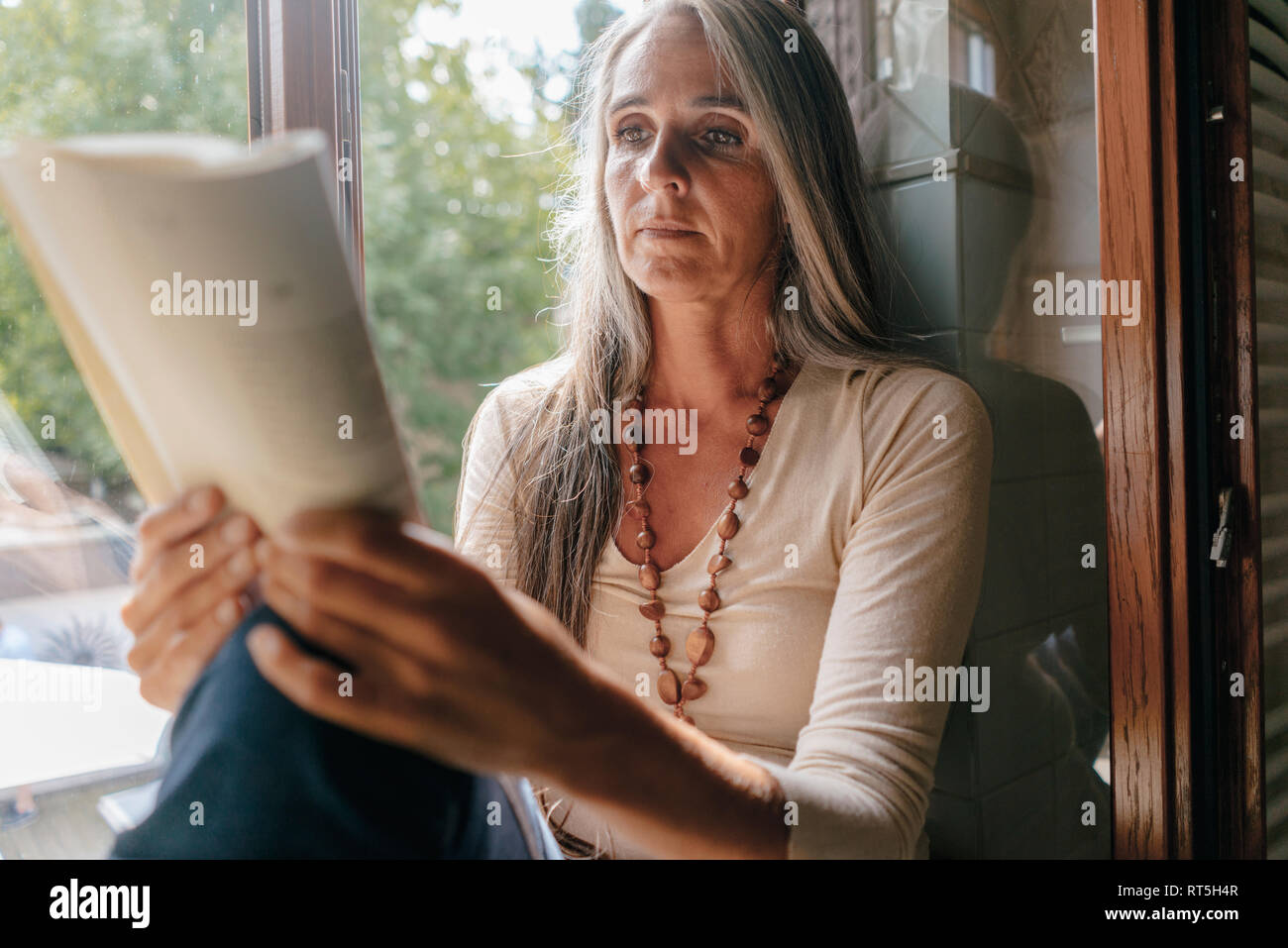 Portrait von Frau auf Fensterbank, zu Hause zu sitzen, ein Buch lesen Stockfoto