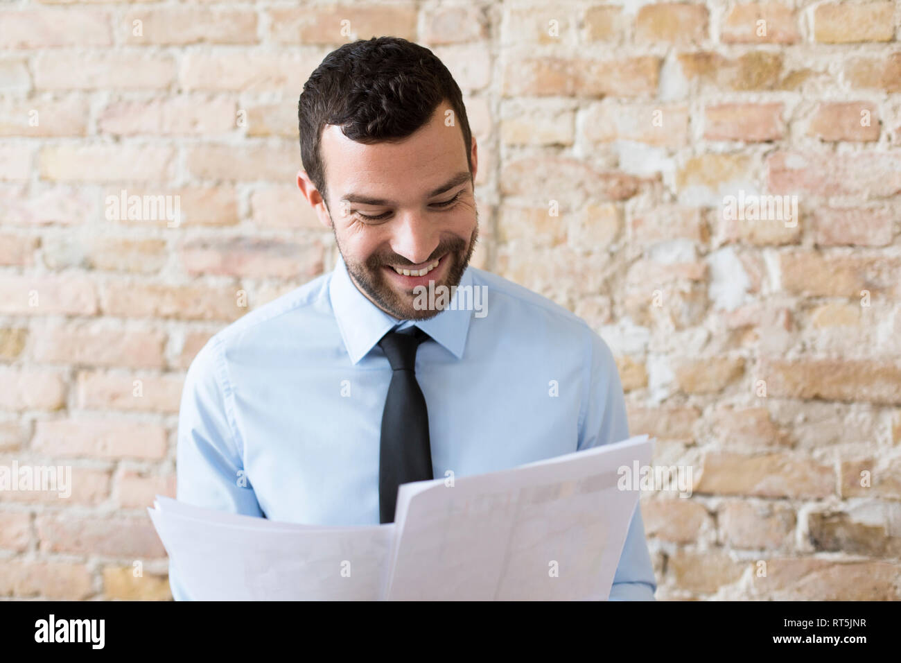 Lächelnd Geschäftsmann Lesung Dokument an der Wand Stockfoto