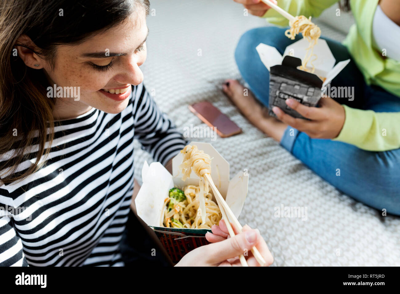 Zwei glückliche junge Frauen, asiatische Essen zum Mitnehmen zu Hause Stockfoto