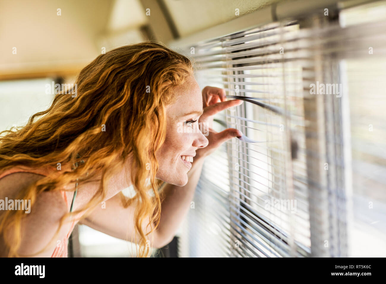 Lächelnde Frau spähen durch Sonnenjalousie Stockfoto