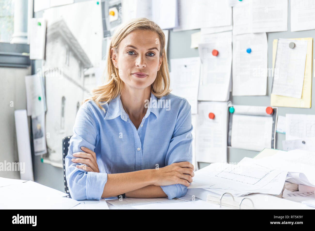 Portrait von selbstbewusste Frau am Schreibtisch im Büro sitzen, umgeben von Schreibarbeit Stockfoto