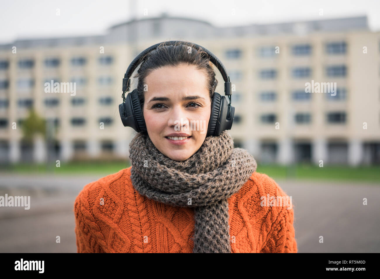 Portrait von lächelnden Frau mit Schal und orange strickpullover Musik hören mit Kopfhörern Stockfoto