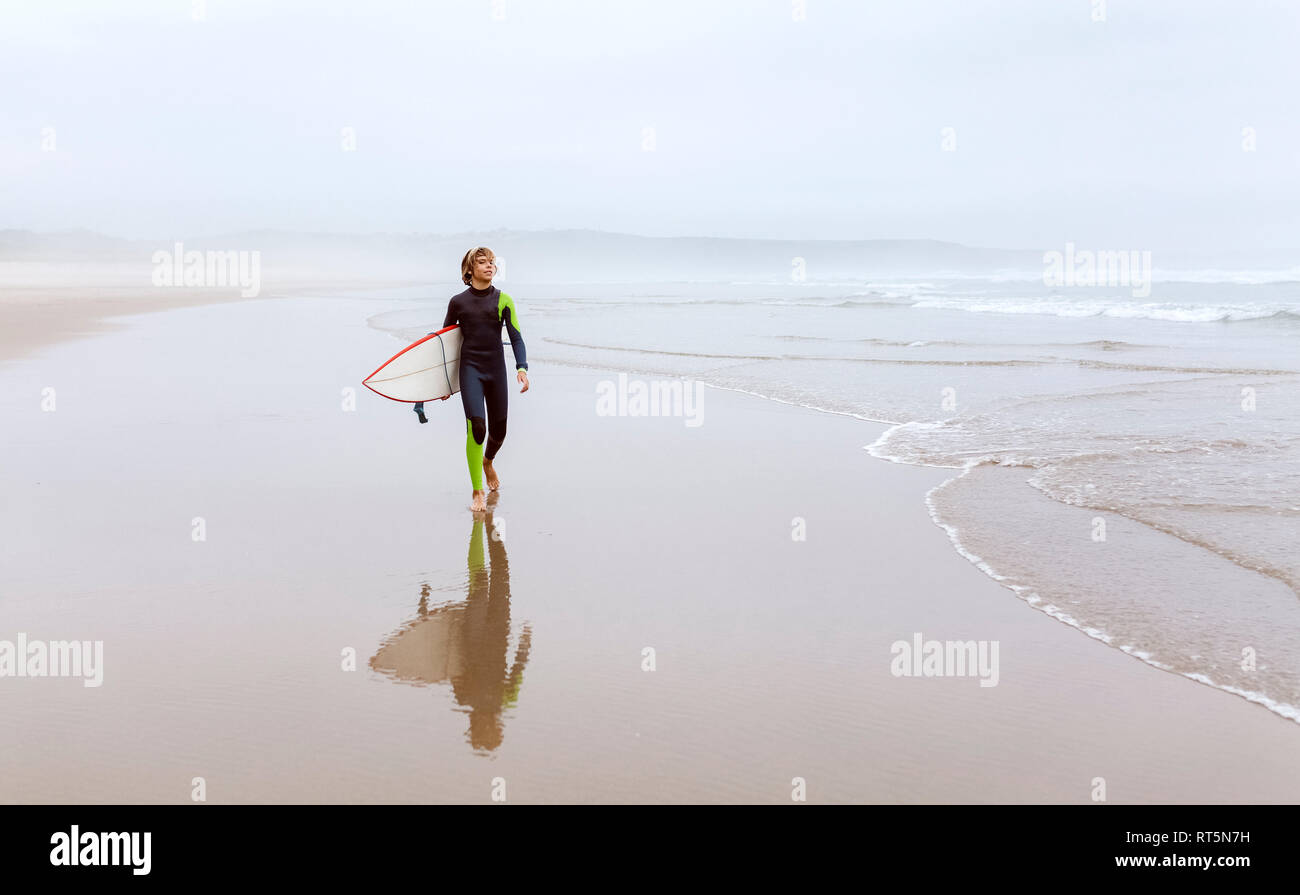 Spanien, Aviles, junge Surfer Surfbrett Durchführung am Strand Stockfoto
