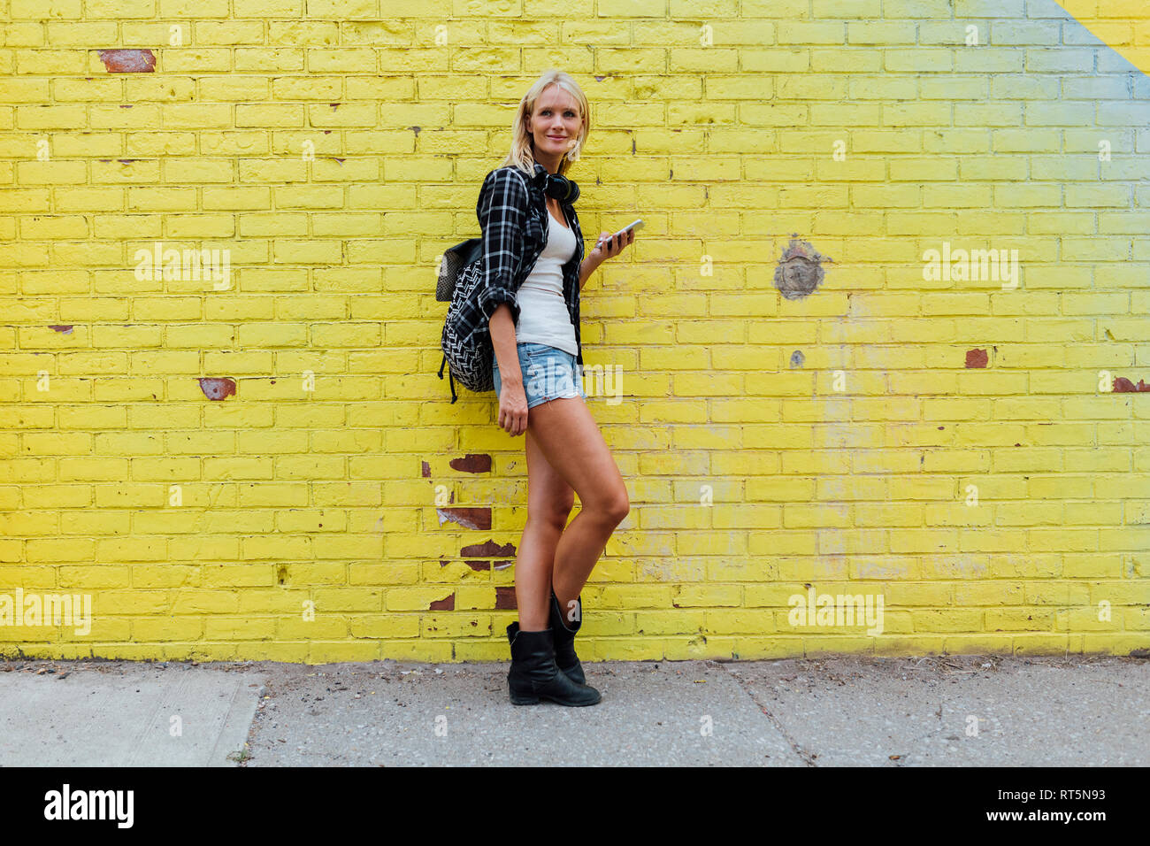 Porträt der jungen Frau mit Handy im yellow brick wall Stockfoto