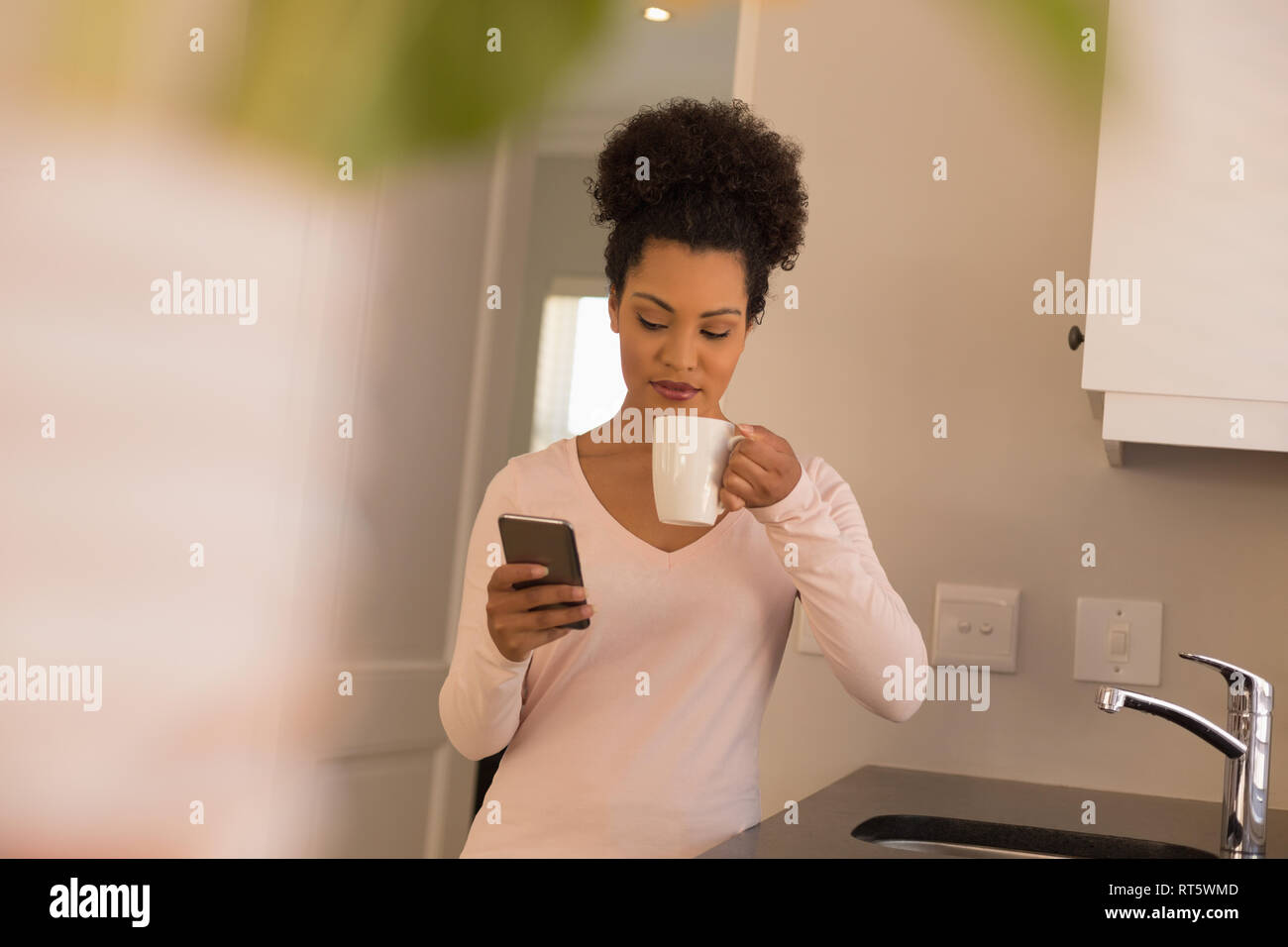 Frau mit Kaffee, während mit Handy in der Küche Stockfoto