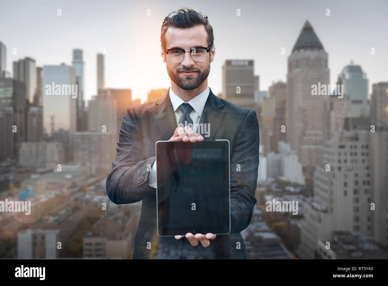 Schauen Sie mal rein! Portrait von fröhlicher junger Mann im Anzug mit digitalen Tablet an Kamera beim Stehen vor der morgen Stadtbild Hintergrund. Digitale Konzept. Smart Business. Technologien Stockfoto