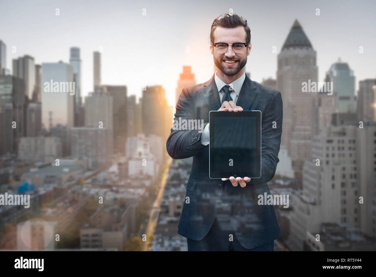 Die Unternehmen vereinfacht. Portrait von fröhlicher junger Mann im Anzug mit digitalen Tablet und lächelnd, während gegen von morgen Stadtbild Hintergrund stehen. Digitale Konzept. Smart Business. Stockfoto