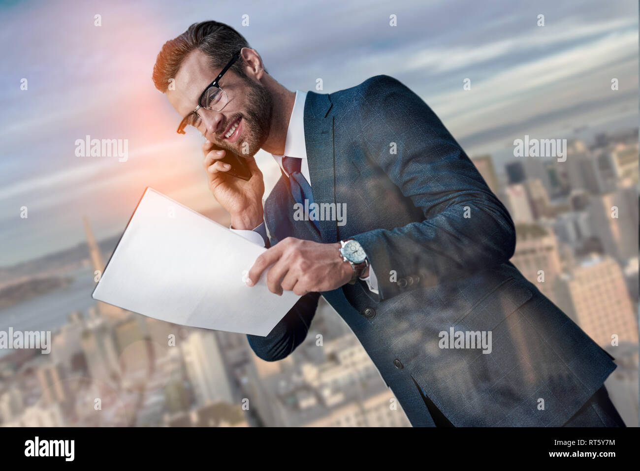 Vertrag über gute Bedingungen. Fröhlicher junger Unternehmer im Gespräch per Telefon und auf Dokumente, während sich gegen schöne Stadtbild Hintergrund. Partnerschaft. Geschäftskonzept. Erfolg Stockfoto