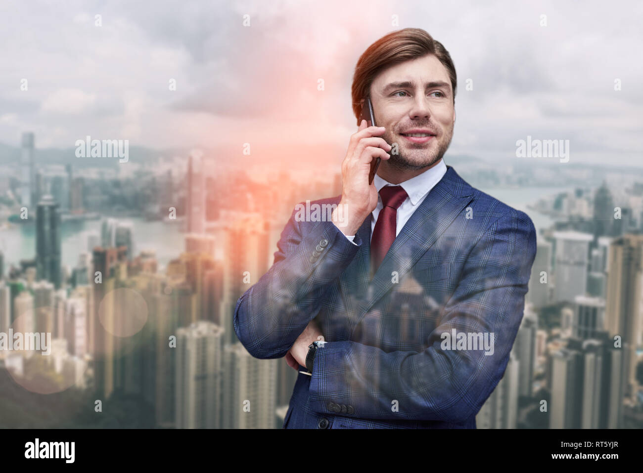 Die guten Nachrichten. Fröhlicher junger Unternehmer im Gespräch per Telefon und lächelnd, während gegen von stadtbild Hintergrund stehen. Kommunikation. Die digitalen Technologien Stockfoto