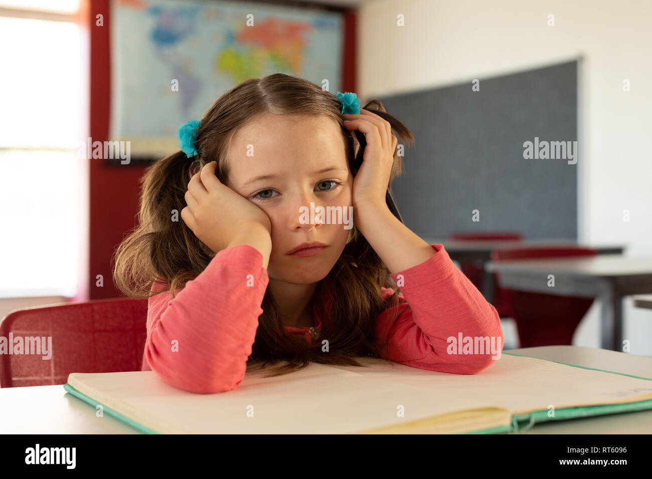 Trauriges Mädchen lehnte sich auf Schreibtisch in einem Klassenzimmer Stockfoto