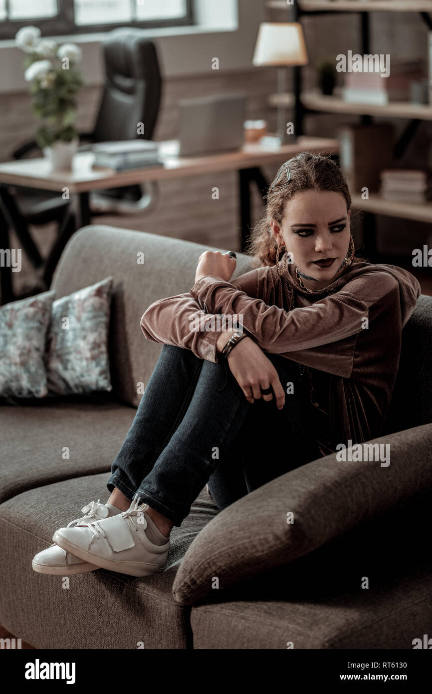 Jeans und Turnschuhe. Teenager in Jeans und Turnschuhe Gefühl pessimistisch Sitzen auf einem Sofa zu Hause Stockfoto