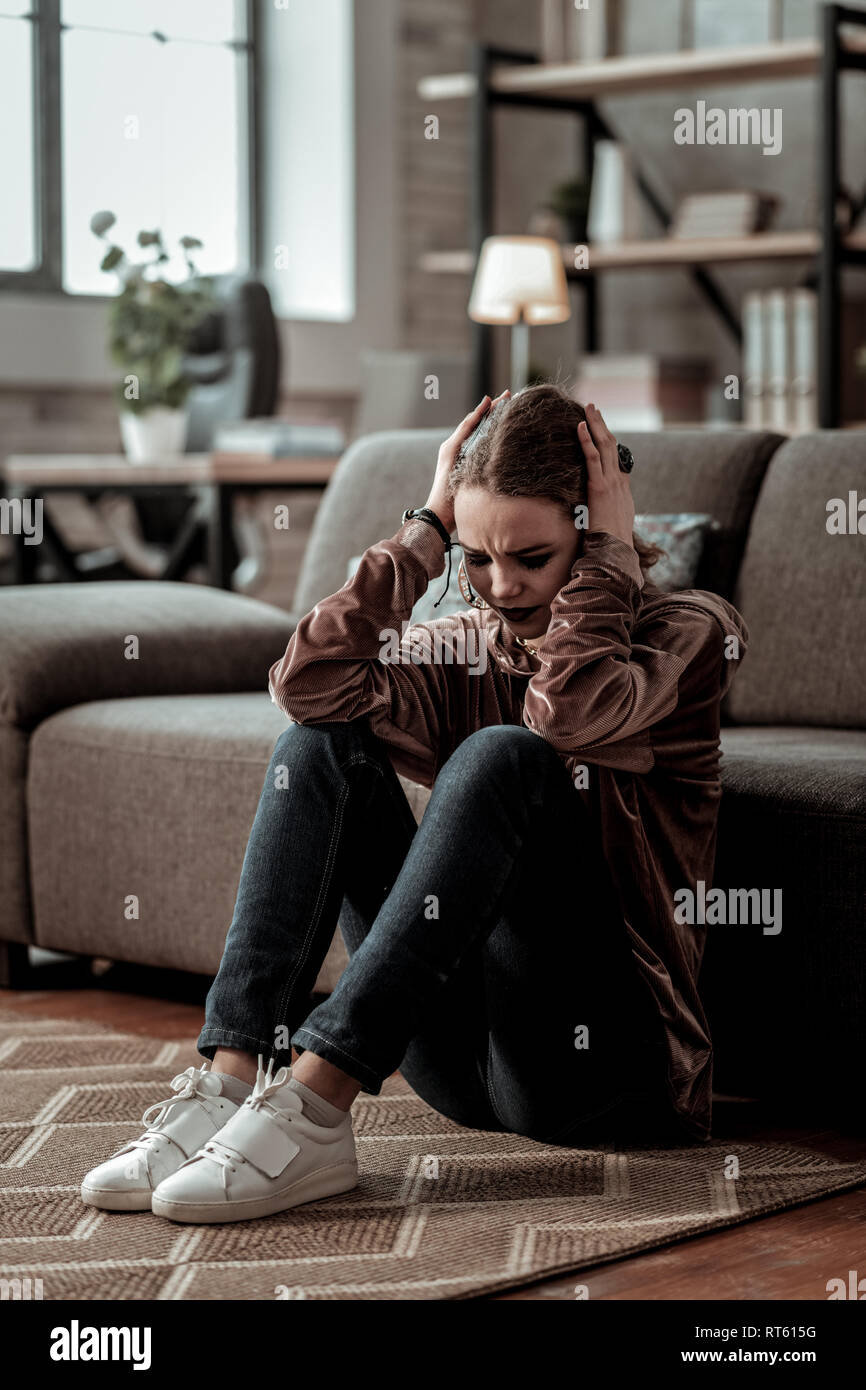 Starke Kopfschmerzen. Junges Mädchen mit starken Kopfschmerzen nach der Großen Depression beim Sitzen auf dem Boden Stockfoto