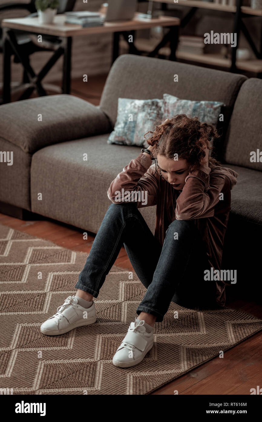 Tiefe Depression. Junges Mädchen mit weißen Sneakers sitzen auf dem Boden, während in tiefe Depression Stockfoto