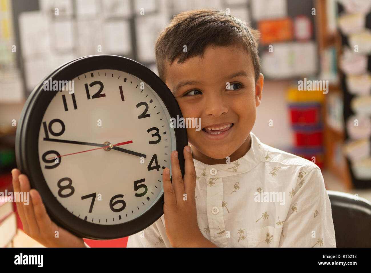 Lächelnden Schuljungen mit Wanduhr weg schauen in einem Klassenzimmer Stockfoto