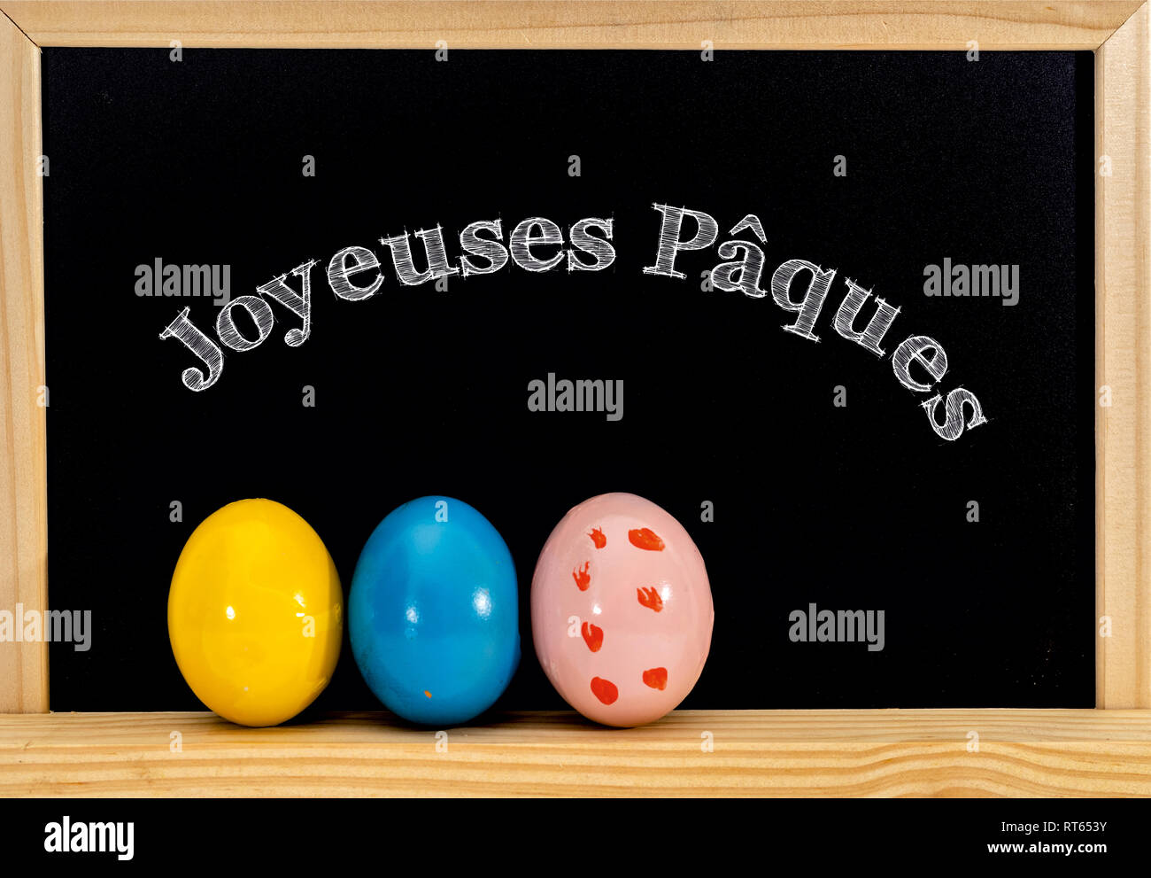 Ostern Rahmen mit bemalten Eiern und Schiefertafel. Frohe Ostern in weißer Kreide. Frohe Ostern in Französisch: joyeuses paques Stockfoto