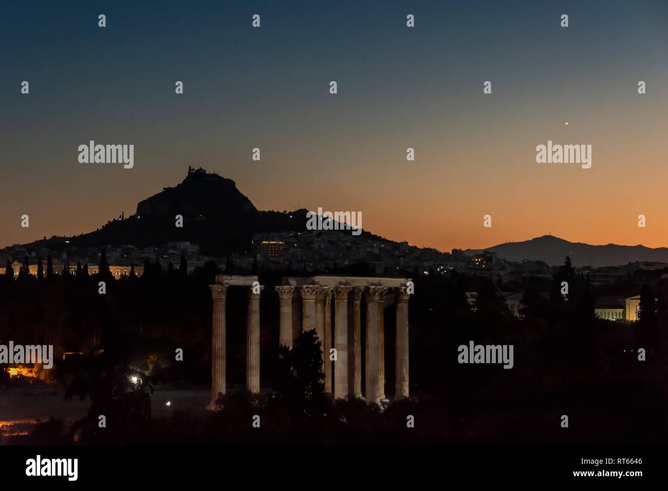 Die Ruinen der Tempel des Olympischen Zeus und den Berg Lycabettus mit Uhrturm und Agios Georgios bei Sonnenuntergang, Athen, Griechenland Stockfoto