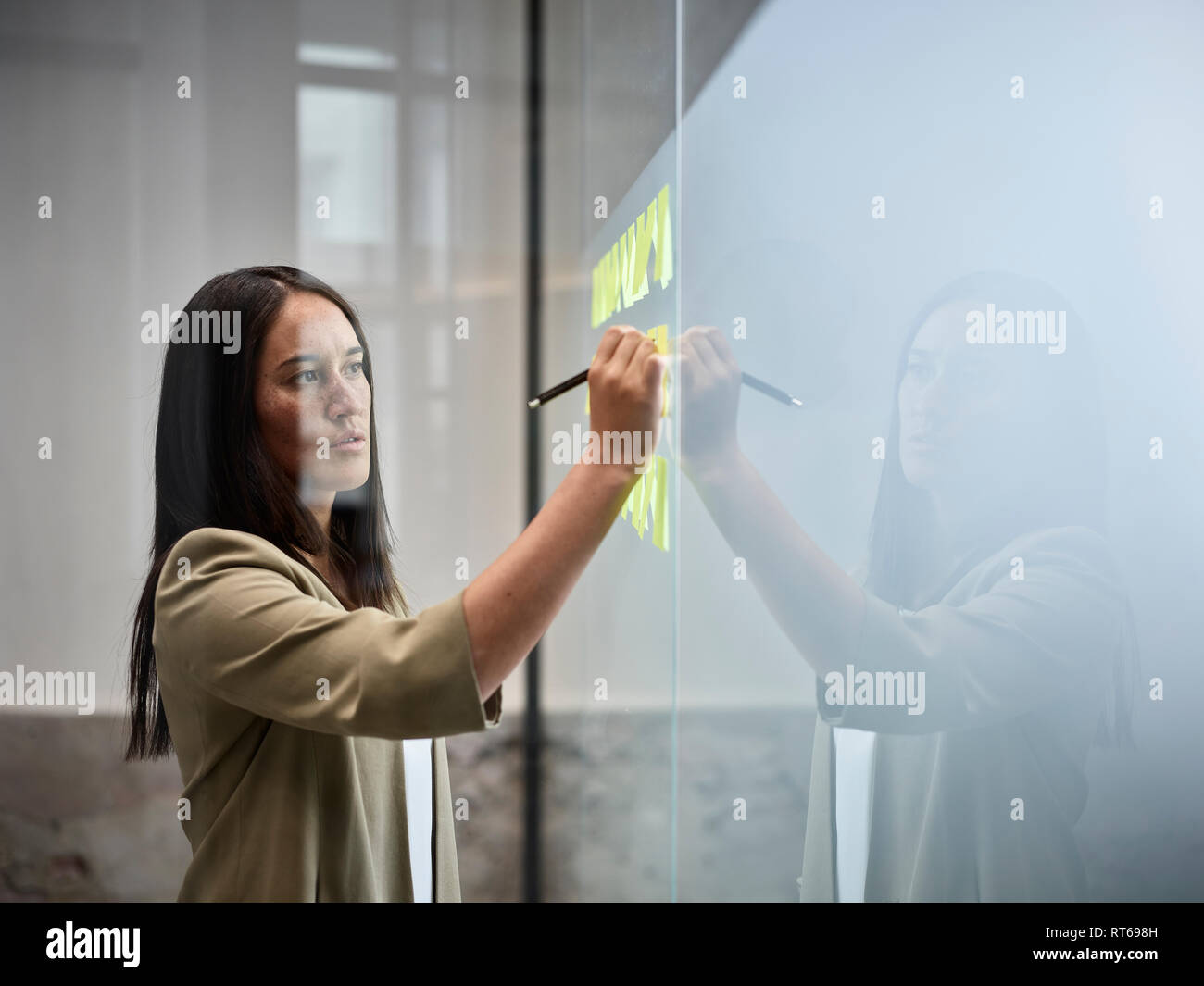 Geschäftsfrau schreiben auf Haftnotizen an der Glasscheibe im Büro Stockfoto