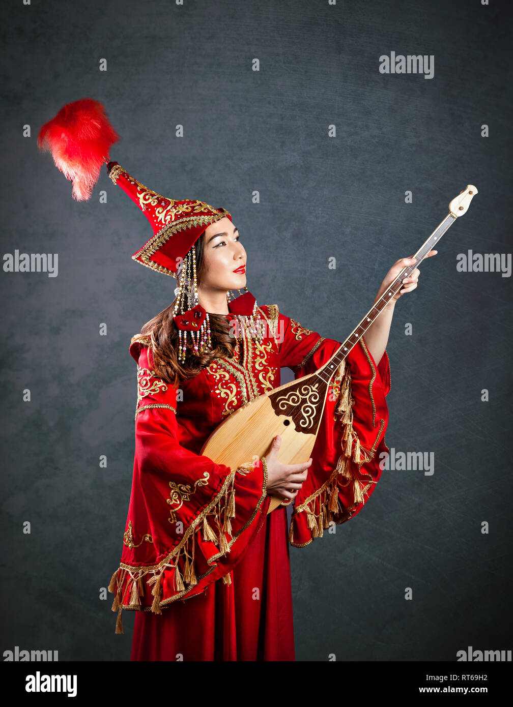 Kasachischen Frau in Rot Kostüm spielen dombra Kasachischen Musical Instrument am grauen Hintergrund Stockfoto