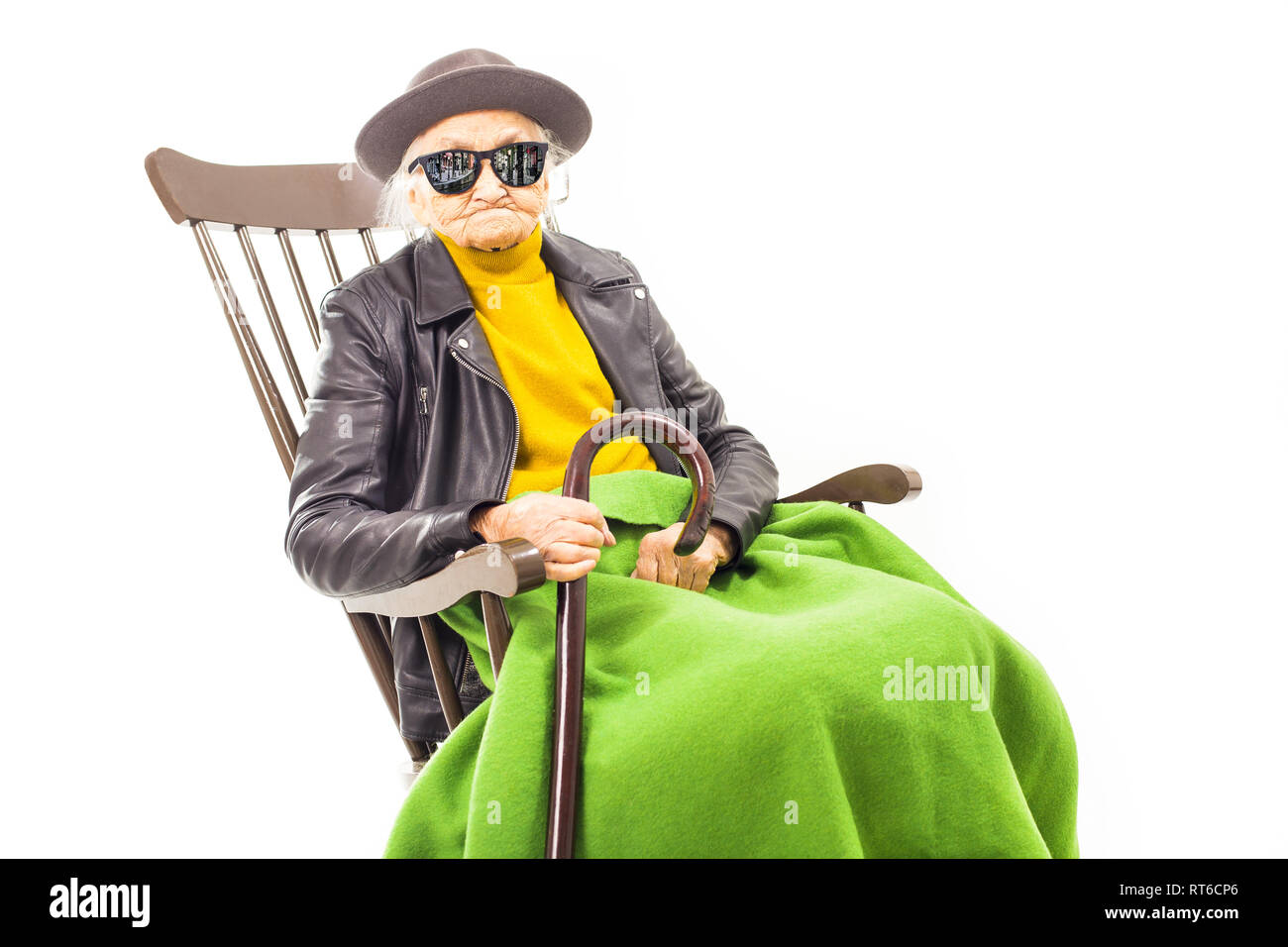 Alte Frau mit Hut und Sonnenbrille auf dem Stuhl verkleidet mit grüner Decke. Stockfoto