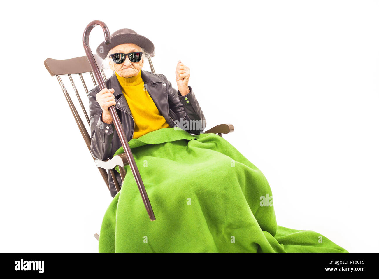 Alte Frau mit Hut und Sonnenbrille auf dem Stuhl verkleidet mit grüner Decke. Stockfoto