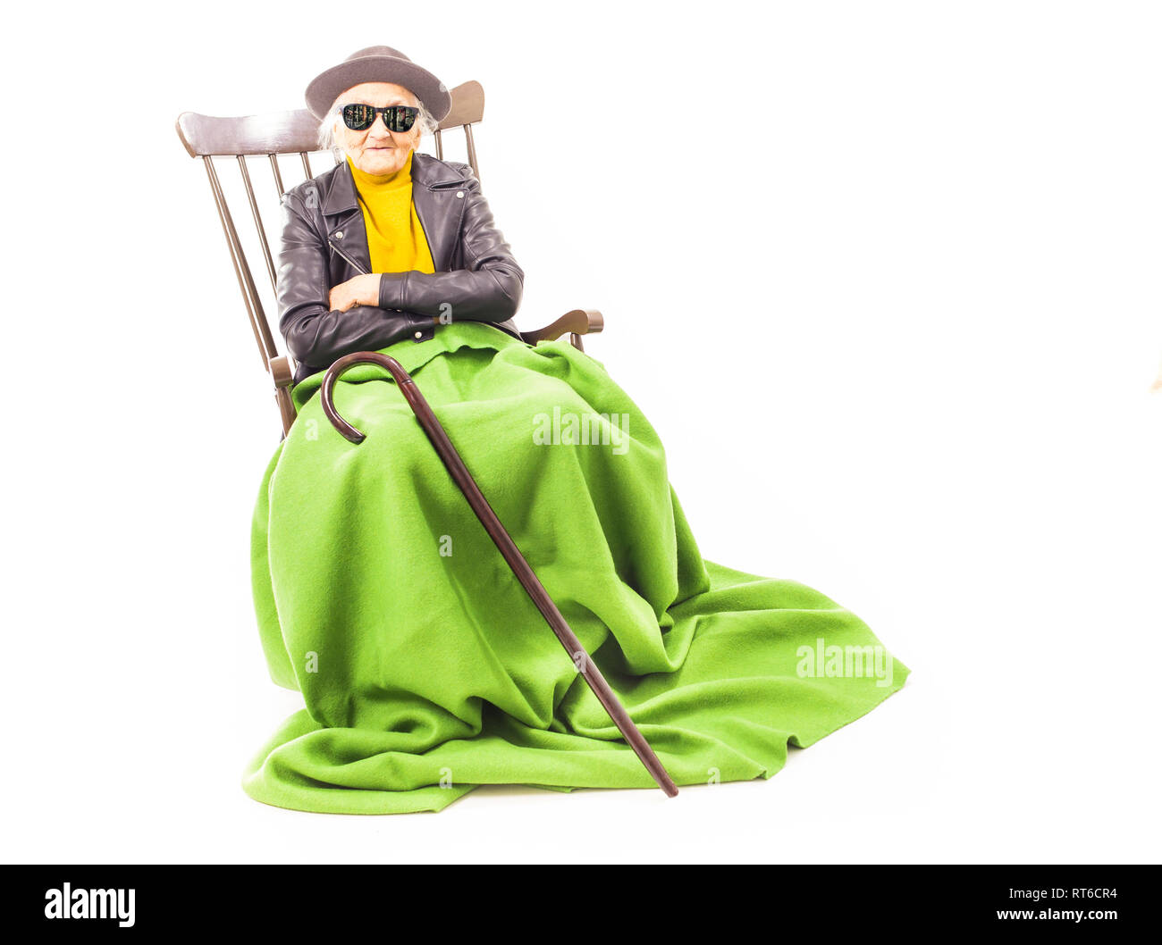 Alte Frau mit Hut und Sonnenbrille auf dem Stuhl verkleidet mit grüner Decke. Stockfoto
