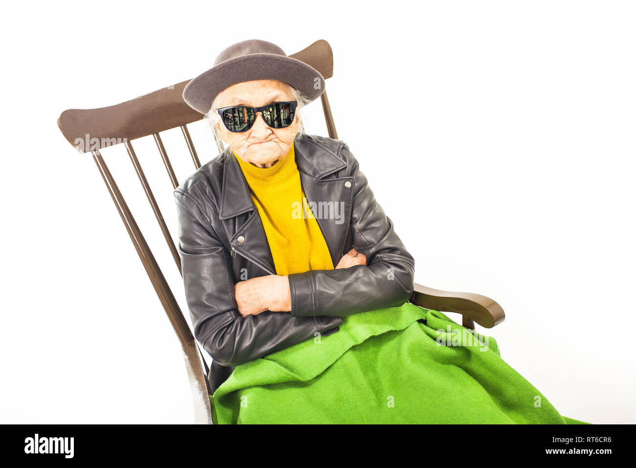 Alte Frau mit Hut und Sonnenbrille auf dem Stuhl verkleidet mit grüner Decke. Stockfoto