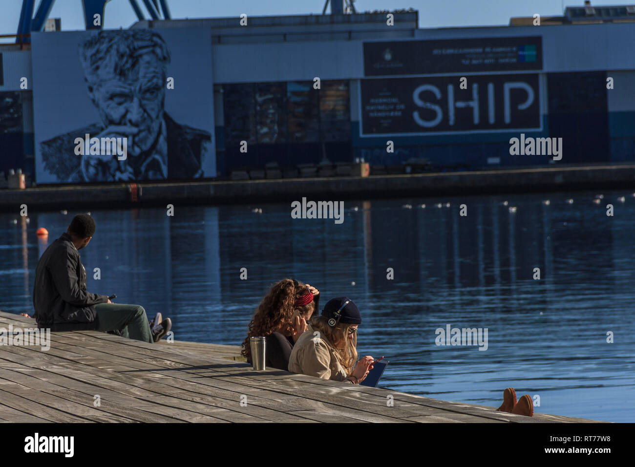 Studenten in der Sonne durch den Hafen während einer Periode des ungewöhnlich warmen Wetter in Aarhus, Dänemark. Die Temperaturen erreichen 16 C obwohl die Februar durchschnittlich 6 ist C. Aarhus, Dänemark. Februar 2019. Stockfoto