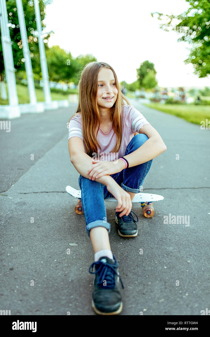 Happy girl Teenager 8-12 Jahre alt, saß auf einem Skateboard. Im Sommer in der Stadt nach der Schule Unterricht auf der Straße. Sport Schülerin Stockfoto
