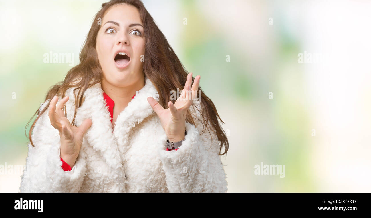 Schöne Übergrößen junge Frau tragen Winter Schafe Mantel über isolierte Hintergrund verrückt und wütenden Schreien und Kreischen mit aggressiven Ausdruck und einer Stockfoto