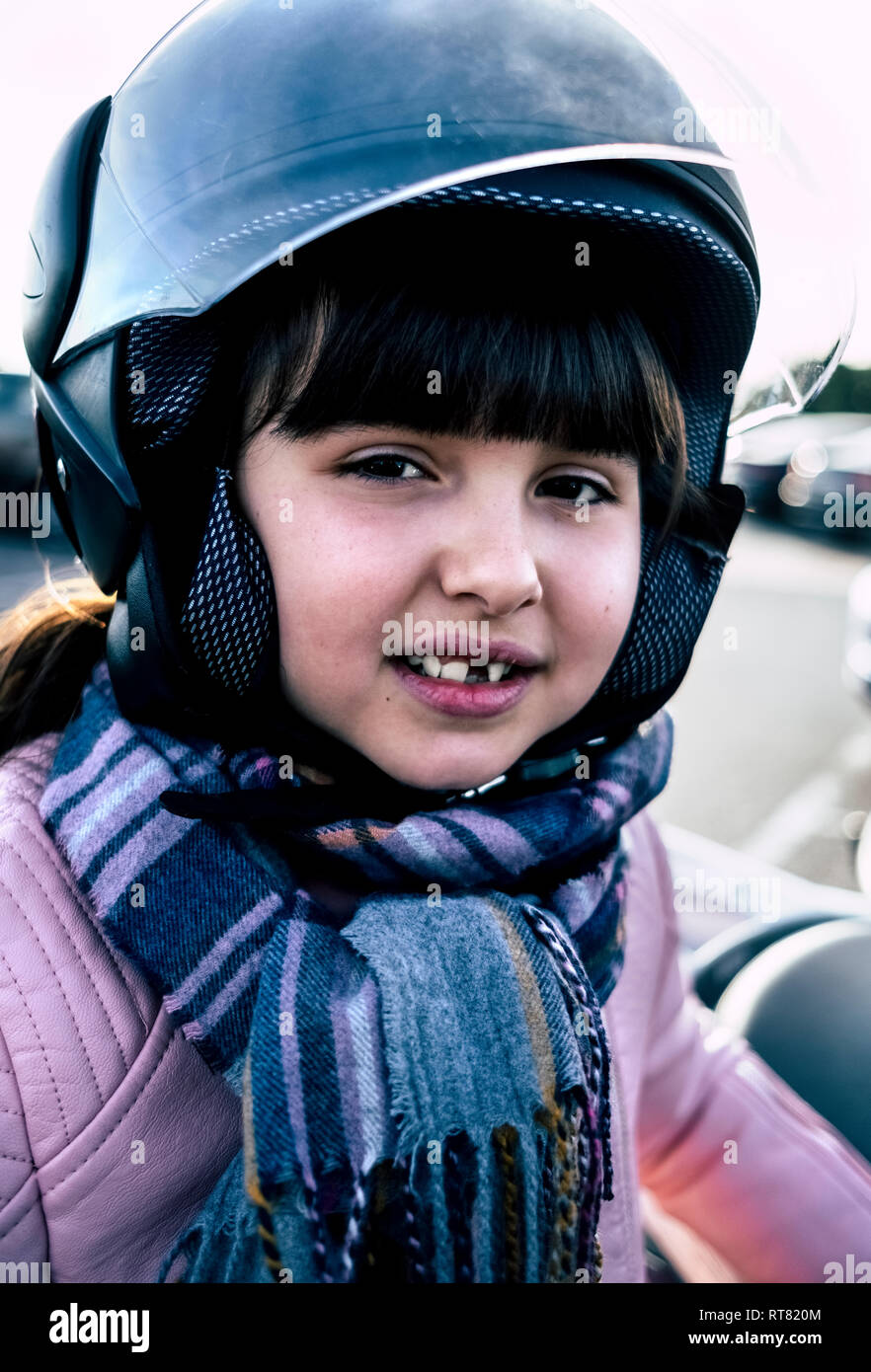 Portrait von kleinen Mädchen mit Zahnlücke tragen Helm auf Motorrad Stockfoto