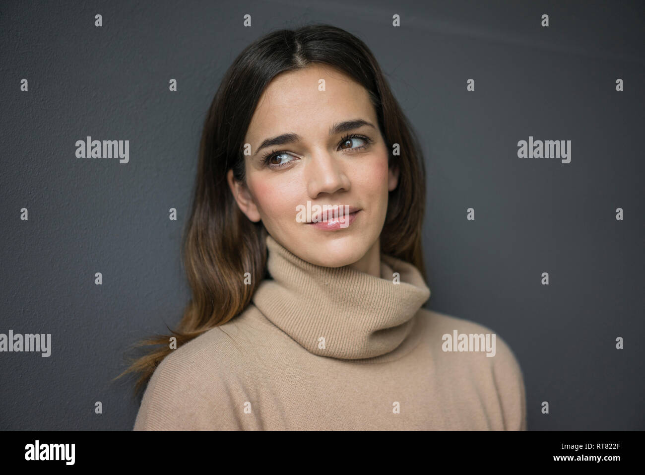 Porträt der lächelnde Frau trägt Hellbraun rollkragen pullover gegen grauer Hintergrund Stockfoto