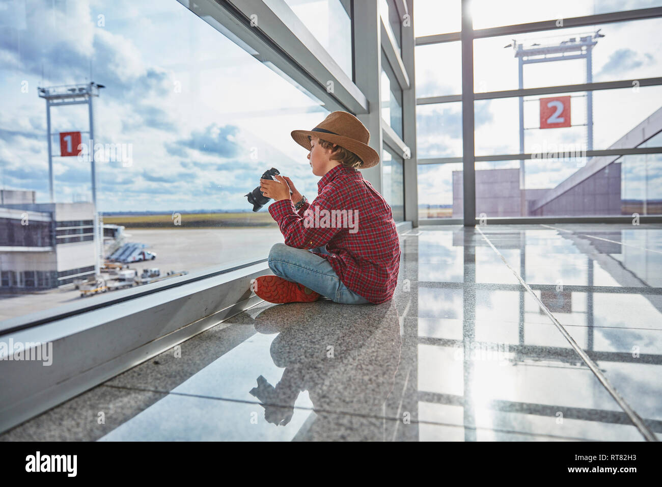 Junge sitzt hinter Fensterglas am Flughafen halten einer Kamera Stockfoto