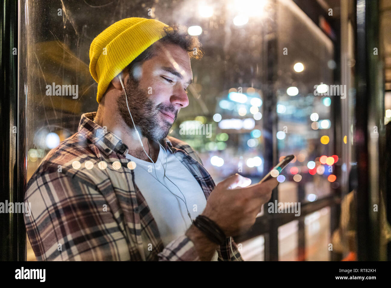 UK, London, lächelnden Mann an der Bushaltestelle bei seinem Telefon suchen Stockfoto