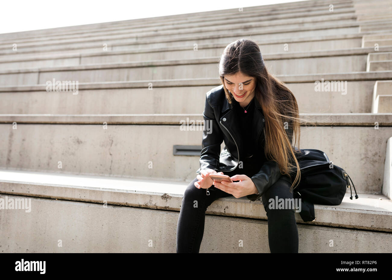 Lächelnde junge Frau sitzt auf der Treppe mit Handy Stockfoto