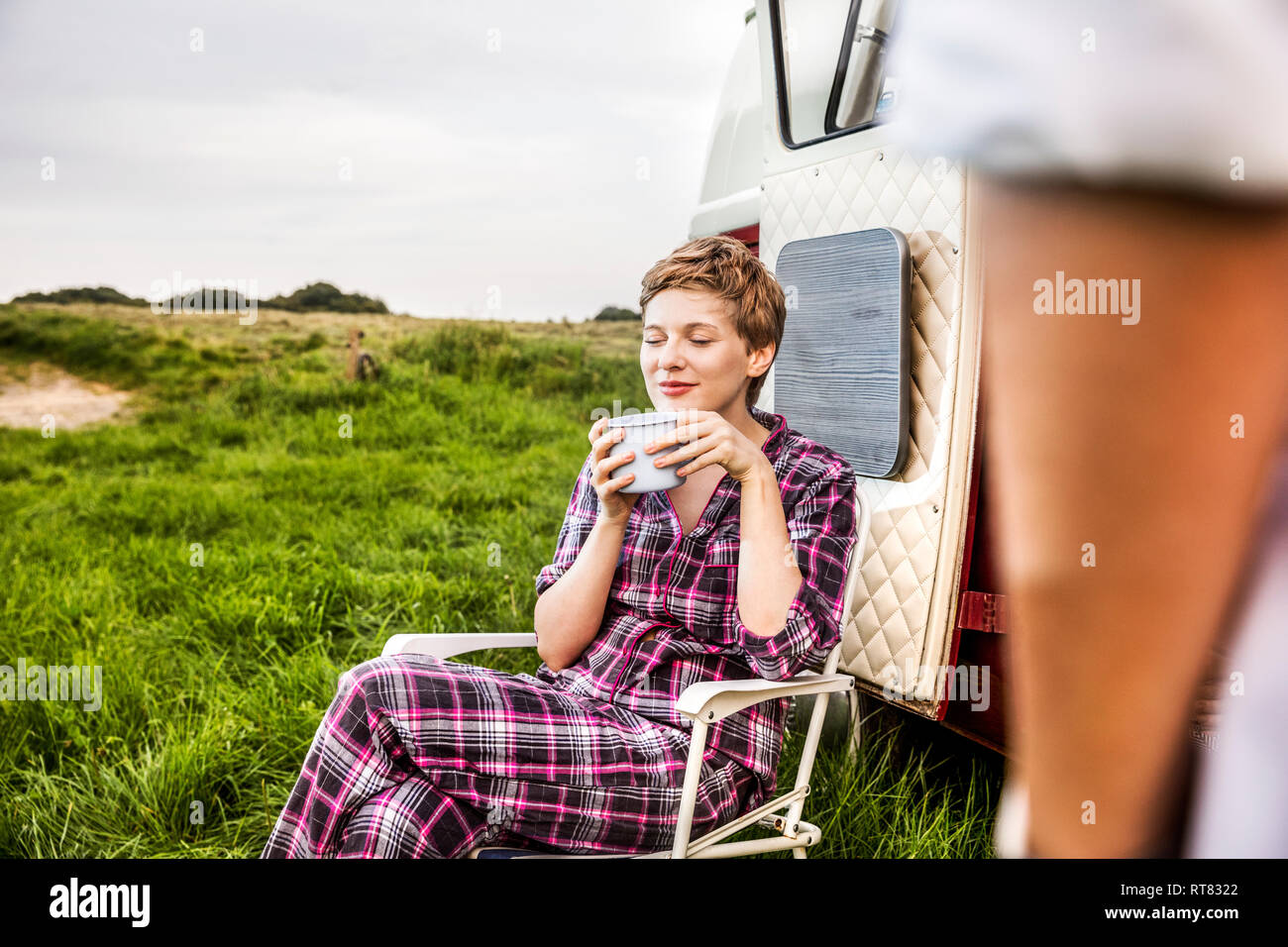 Frau in Pyjama genießen Sie Kaffee in einem Van in ländlichen Landschaft Stockfoto