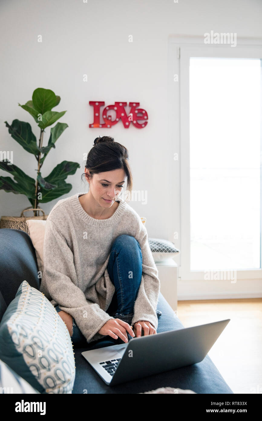 Frau sitzt auf dem Sofa, im Internet surfen, mit Laptop Stockfoto