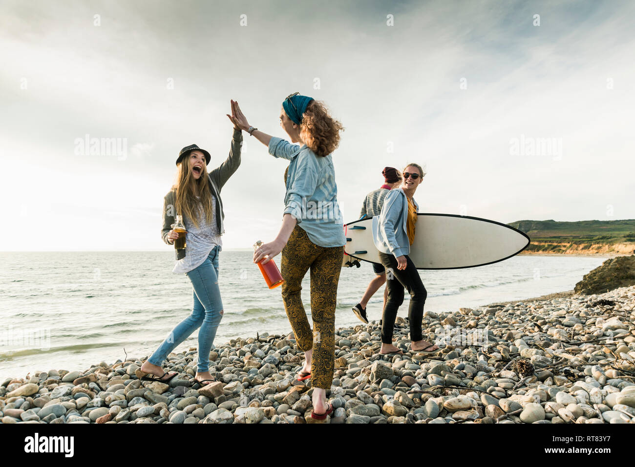 Aufgeregt Freunde mit Surfbrett und Getränke auf steinigem Strand Stockfoto