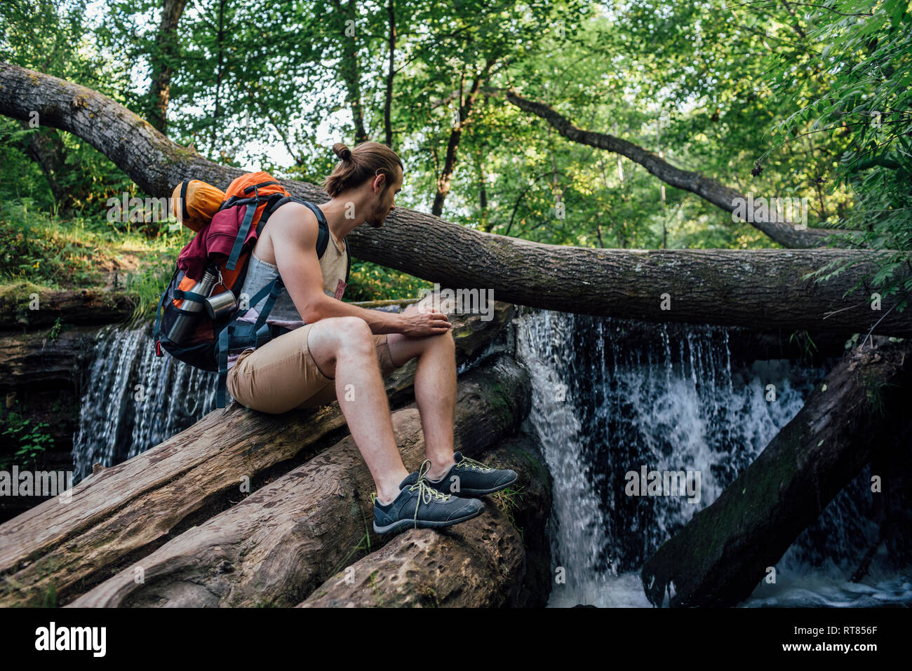 Junger Mann mit Rucksack in eine Pause in einem Wald in der Nähe von Wasserfall Stockfoto