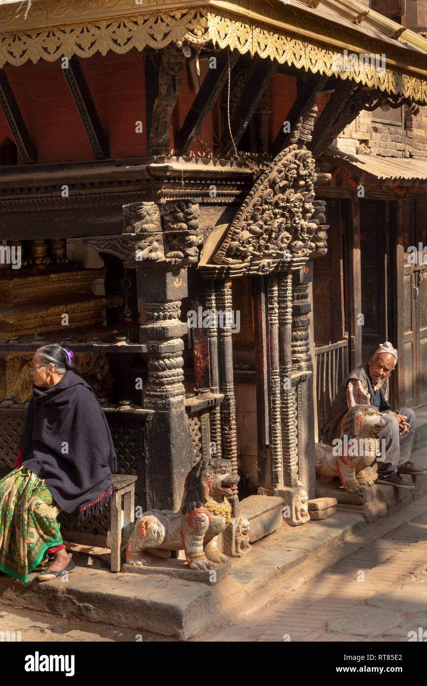 Nepal, Kathmandu Tal, Bhaktapur, Bangsagopal Nasamana, alte Mann und die Frau in der Sonne sitzen, kunstvoll geschnitzten alte hölzerne Tempel Stockfoto