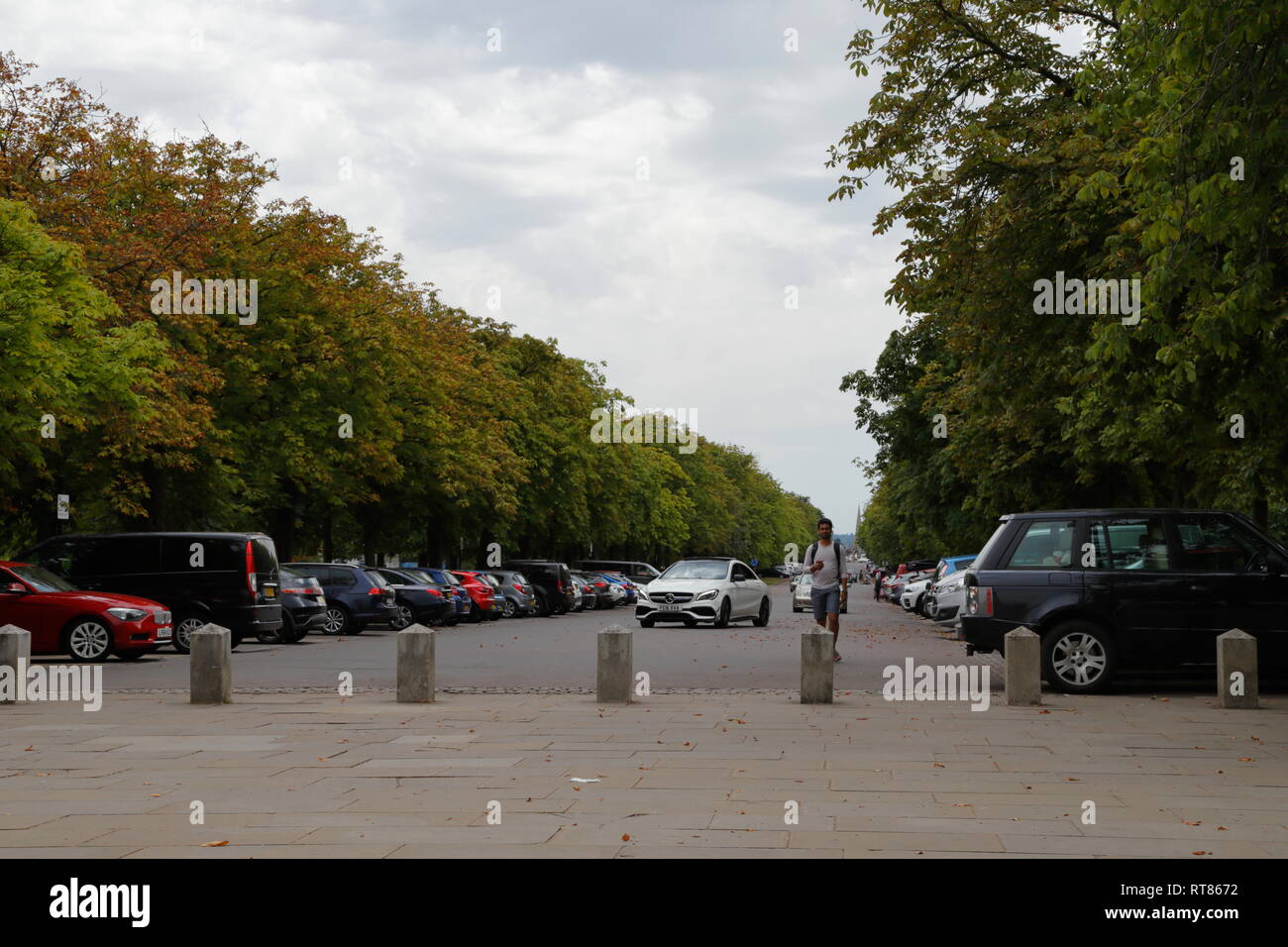 Ein Mann Spaziergänge entlang wie Autos kommen auf einem Parkplatz zu parken (Parkplatz) in Greenwich in London, Vereinigtes Königreich. Stockfoto