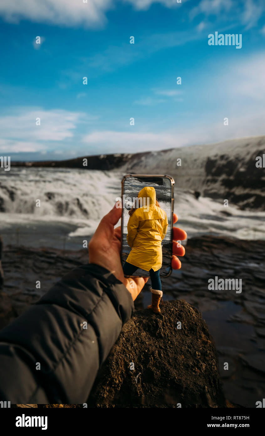 3D-Montage der Mann unter Smartphone Bild der isländischen Landschaft und Frau tragen gelbe Regenmantel Stockfoto