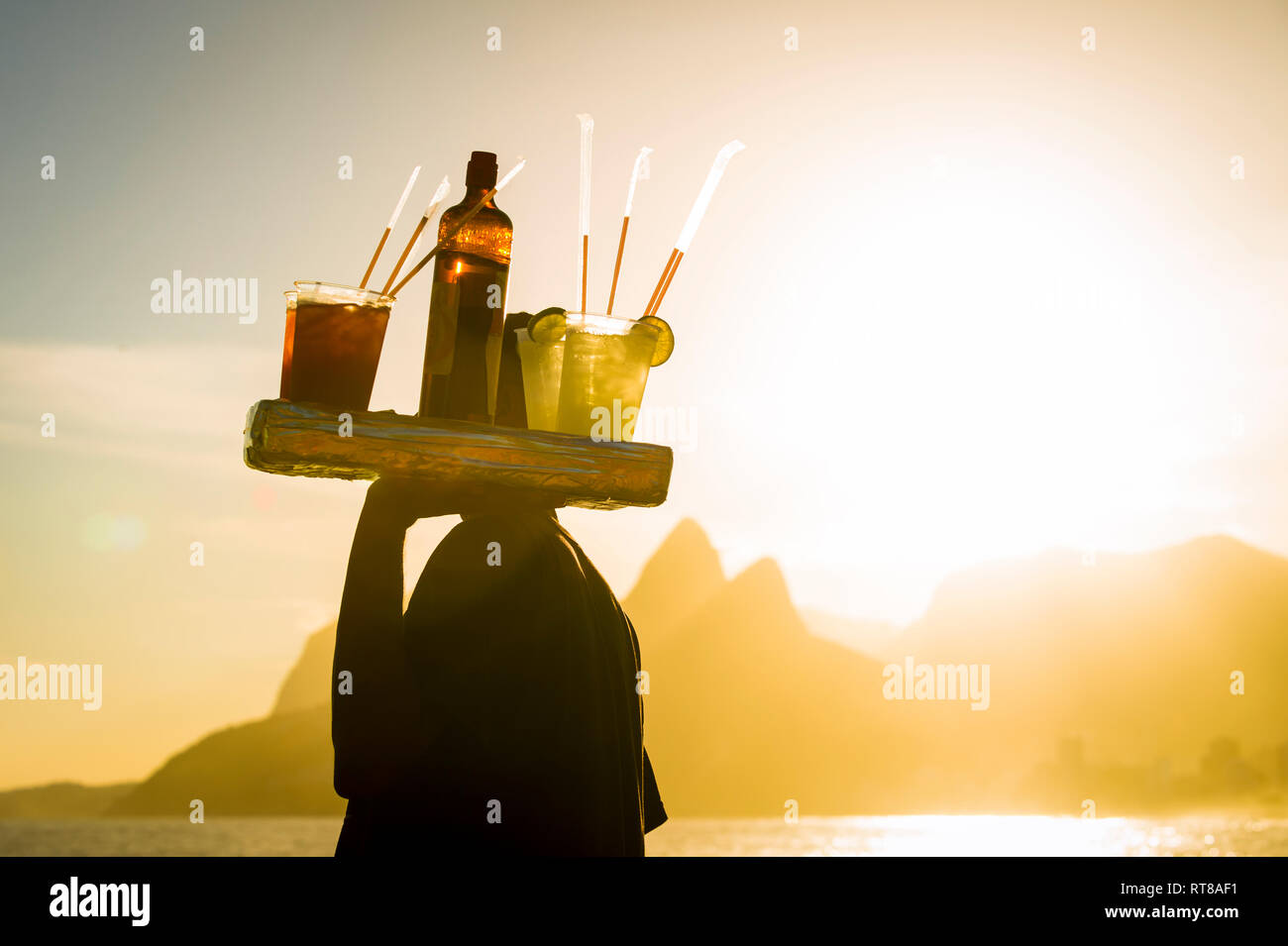 Einen herrlichen Blick auf den Sonnenuntergang mit einem unkenntlich Silhouette einer Strand Anbieter Durchführung caipirinha Cocktails in Silhouette in Ipanema, Rio de Janeiro Stockfoto